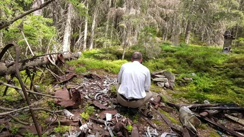 Man examining rusted plane crash wreckage on mountain forest slope Stock Footage 344886717
