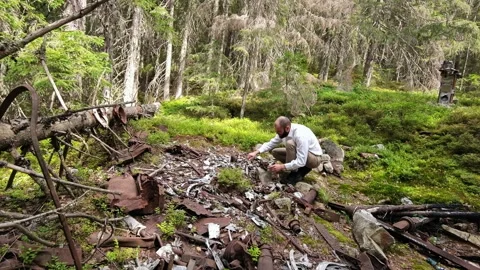 Man examining rusted plane crash wreckage on mountain forest slope Vídeo Stock 344886826