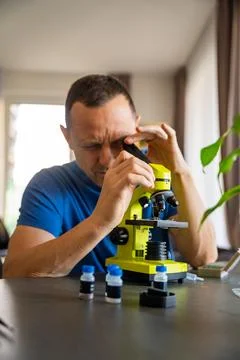 Man examining various samples under a microscope at home as a hobby. Concept of Stock Photos