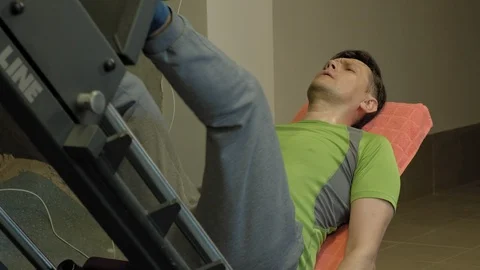 A man with excess weight doing leg presses on the simulator in the gym. Fitness Stock Footage 107506174