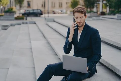 Man executive worker talks on cellphone with business partner uses modern laptop Stock Photos
