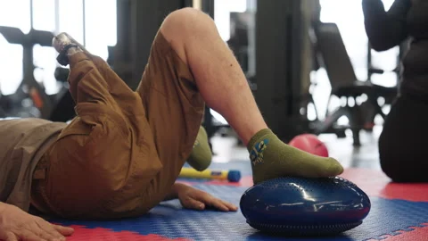 Man exercises on a balance tool while another person observes in a gym setting Stock Footage 345147098