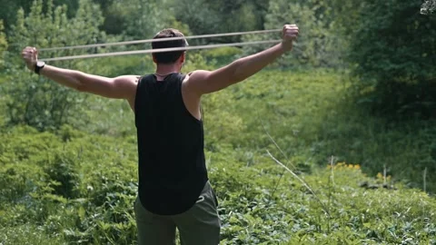 A man exercises in an outdoor setting using a resistance band. He is performing Stockbeeldmateriaal 339016594