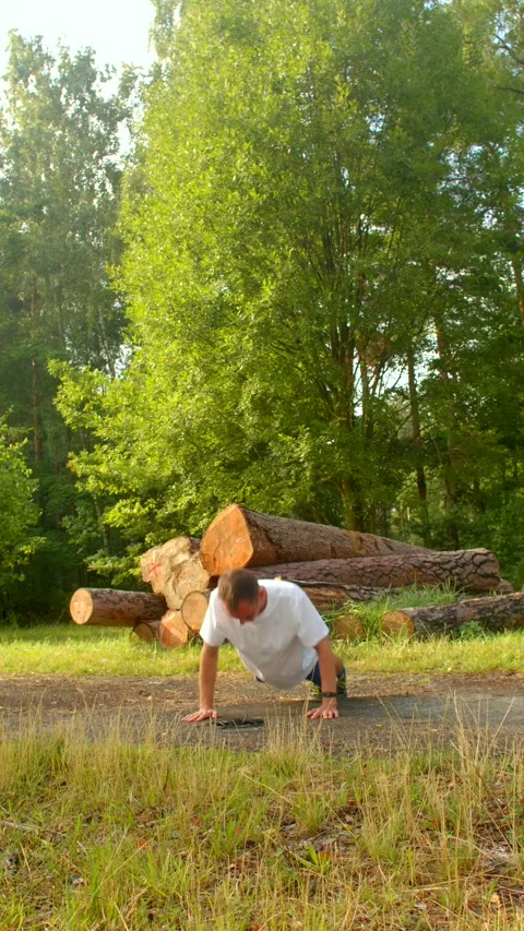 A man exercises outdoors, doing pushups in a tranquil forest Vídeos de archivo 314346028