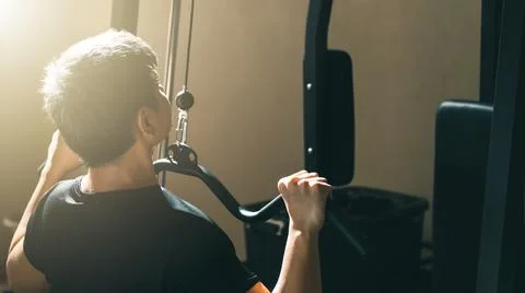 Man exercising on cable machine, strengthening body in gym, back view. Stock Photos