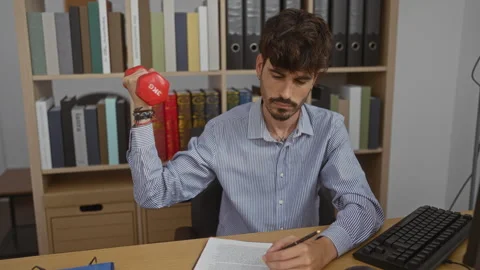 Man exercising with dumbbell and reading document in office, emphasizing mu.. Stock Footage 281812109