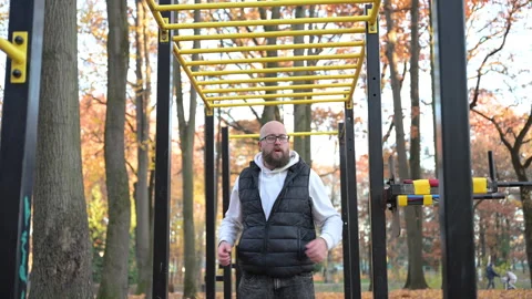 Man exercising on monkey bars in vibrant autumn park, enjoying natures beauty Stock Footage 346768400