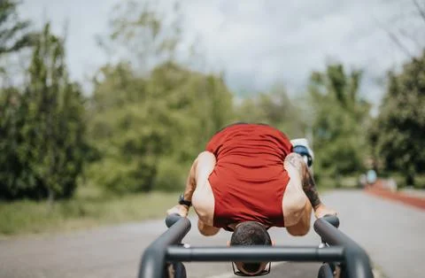 Man exercising outdoors on parallel bars in a sunny park Stock Photos