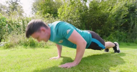 Man exercising outdoors, performing push-ups on grass in sunny park Stock Footage 345571357