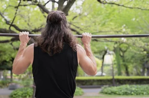 Man exercising on pull-up bar in outdoor park setting Stock Photos
