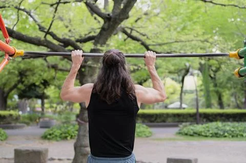 Man exercising on pull-up bar in outdoor park setting Stock Photos