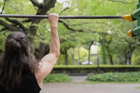 Man exercising on pull-up bar in outdoor park setting Stock Photos