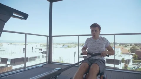 Man exercising with a rowing machine on a rooftop Stock Footage 170885338