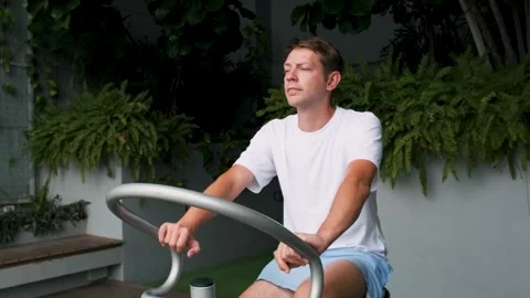 Man exercising on spinning bicycle on modern outdoor balcony with green space Stock Footage 282923523