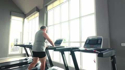 Man exercising on a treadmill in a bright modern gym, sunlight streaming Video stock 318442509
