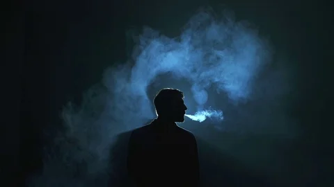Man exhale electronic cigarette smoke against the dark background Stock Footage 69761656
