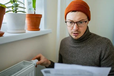 Man experiencing the effects of energy crisis at home, looking shocked and Stock Photos