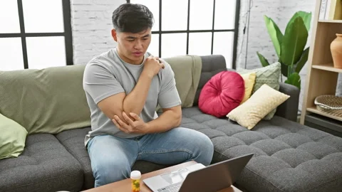 A man experiencing elbow pain while working on a laptop in a modern living .. Stock Footage 274720912