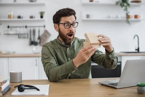 Man experiencing pleasant shock while unpacking parcel box 库存照片