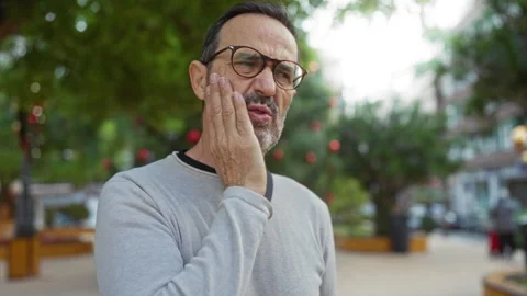 Man experiencing toothache in urban park, mature male with glasses holding .. 스톡 동영상 310641866