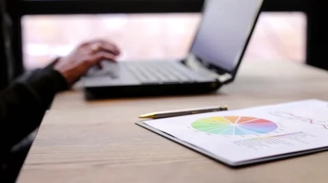 A man exploring on a laptop, and the statistics printed on paper Stock Footage 62590629