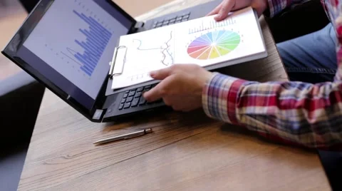 A man exploring on a laptop, and the statistics printed on paper Video stock 63217924