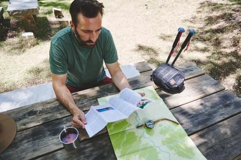 Man Exploring Outdoors With Map and Compass on Wooden Table in Sunny Park Stock Photos