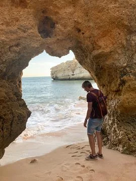 Man exploring a secluded beach through a natural rock archway in Algarve, P.. Stock Photos
