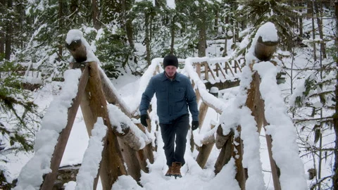 Man Exploring Snowy Forest Crossing Wood Footbridge Stock Footage 304965382