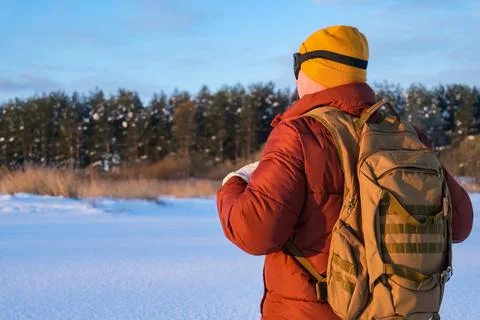 Man exploring snowy wilderness with backpack on frozen lake near forest, wi.. Stock Photos