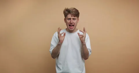 Man expresses strong emotions while standing against a plain wall in a studio Vídeo Stock 328247065