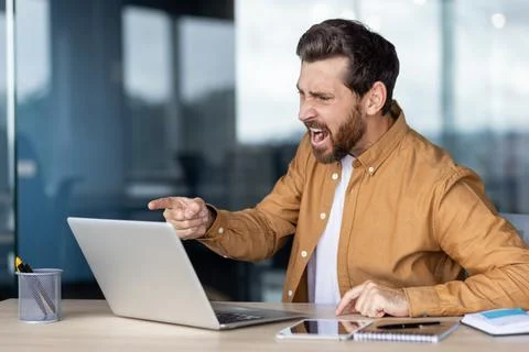 Man expressing frustration at work while using a laptop in an office Stockfoto's