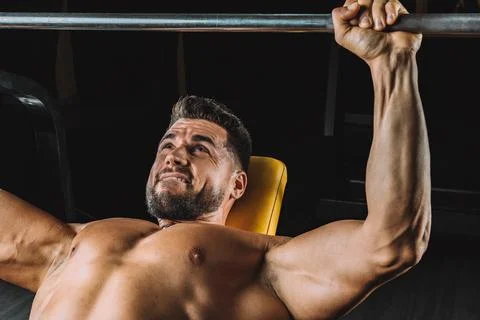 Man with an expression of strength doing bench presses indoors Stock Photos