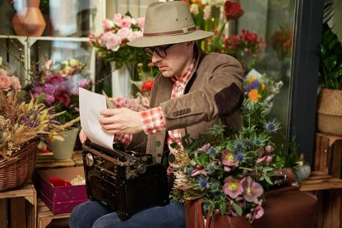 Man in eyeglasses and hat using typewriter in flower shop Stock-Fotos