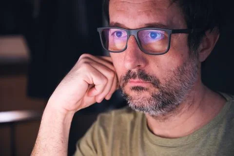 Man with eyeglasses looking at computer screen in dark room, reflection of .. Stock Photos