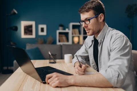 Man in eyeglasses making notes while working on laptop Stock Photos