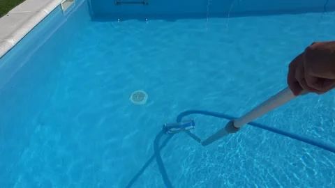 Man, face hidden, vacuums the bottom of a backyard swimming pool, handling .. Stock-Footage 341755499