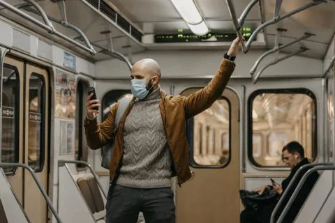 Man in face mask to avoid the spread of coronavirus is using phone in subway  Stock Photos
