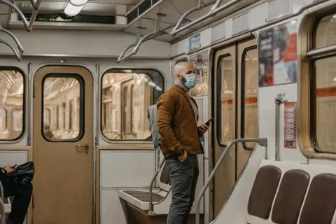 Man in face mask to avoid the spread of coronavirus is using phone in subway  Stock Photos