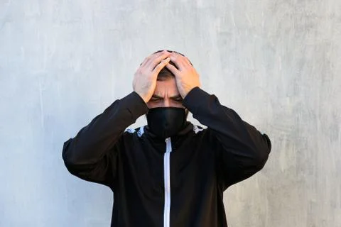 A man in a face mask is holding his head. Fear of getting the crown virus. Stock Photos
