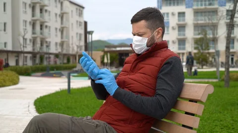 Man in a face mask sits on a bench and looks at the street Stock Footage 127794644