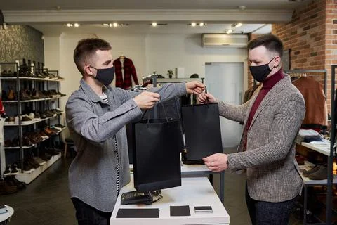 A man in a face mask is taking his purchases from a shop assistant in a store 스톡 사진