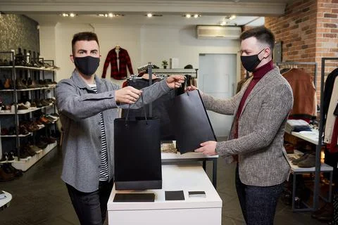 A man in a face mask is taking his purchases from a shop assistant in a store Stock Photos