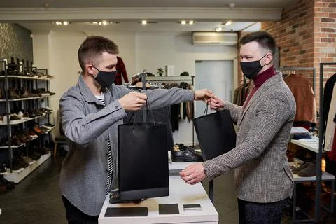 A man in a face mask is taking his purchases from a shop assistant in a store Stock Photos