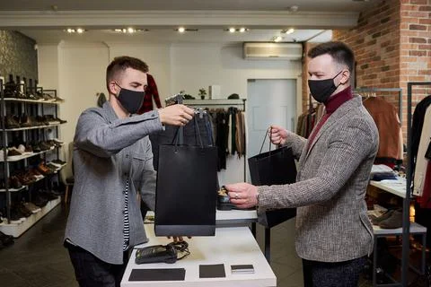 A man in a face mask is taking his purchases from a shop assistant in a store 스톡 사진