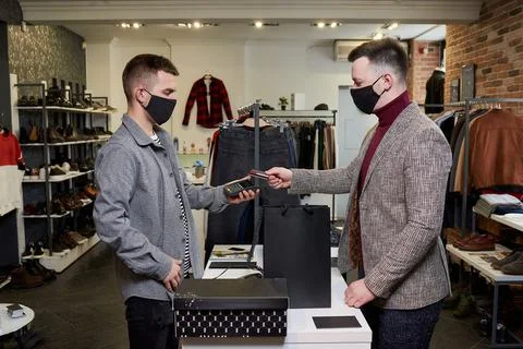 Man in a face mask is using a credit card to pay by NFC for purchases in a st Stock Photos