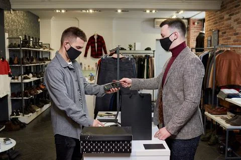 Man in a face mask is using a credit card to pay by NFC for purchases in a st Stock Photos