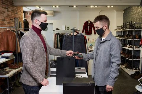Man in a face mask is using a credit card to pay by wireless NFC technology f Stock Photos