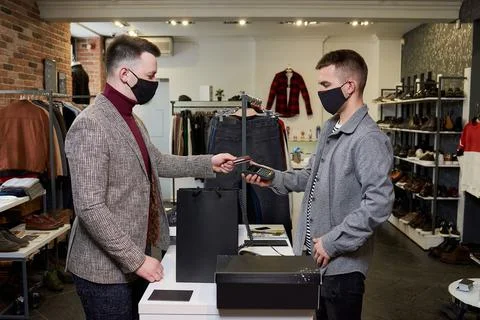 Man in a face mask is using a debit card o pay by wireless NFC technology for Stock Photos