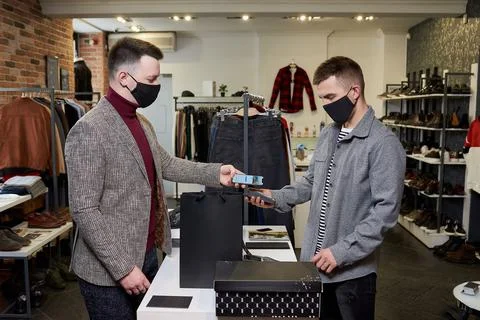 Man in a face mask is using a smartphone to pay by NFC for purchases in a sto Stock Photos
